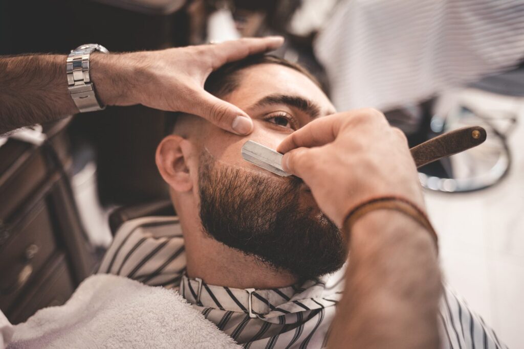 Barbier qui trace le contour d'une barbe courte au rasoir droit