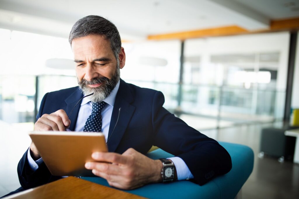 Homme en costume à la barbe courte grisonnante, au travail sur une tablette