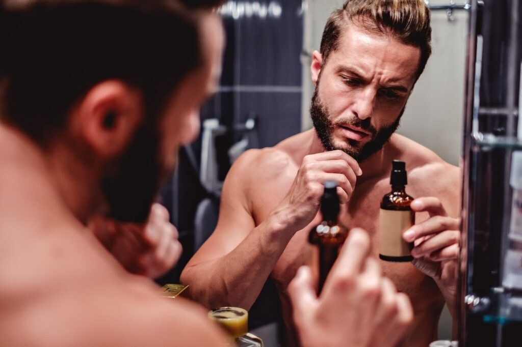 Homme examinant un flacon d'huile à barbe devant le miroir de sa salle de bain