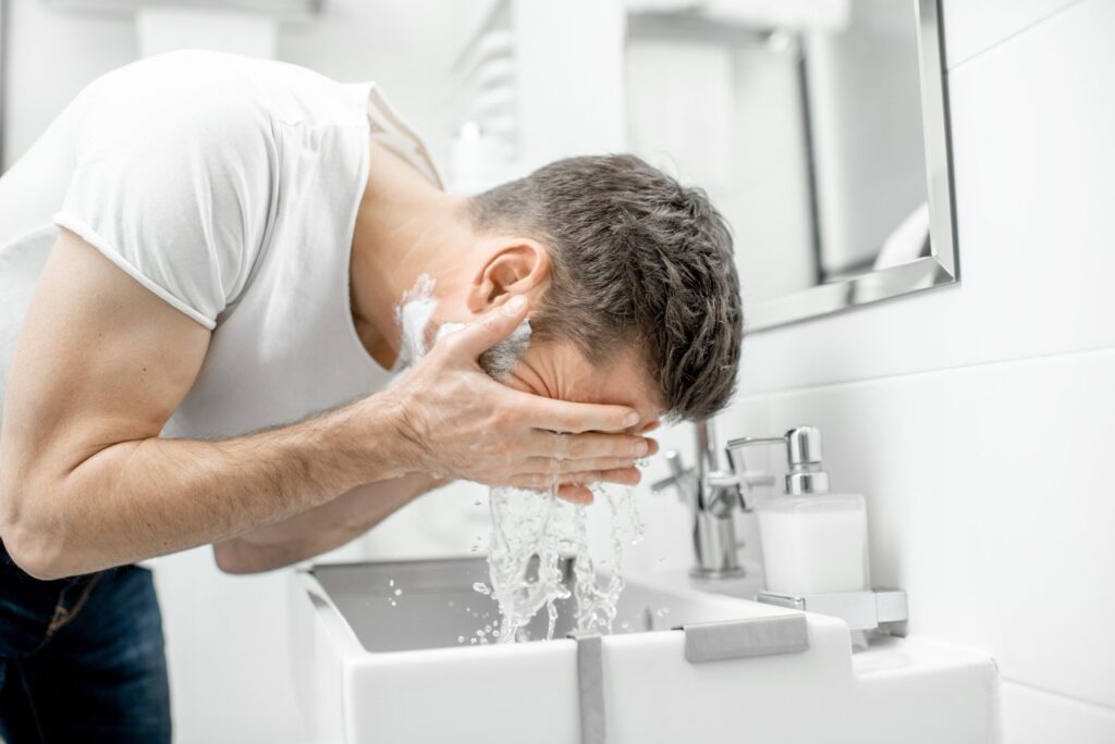 Homme penché sur un lavabo qui se rince le visage à l'eau