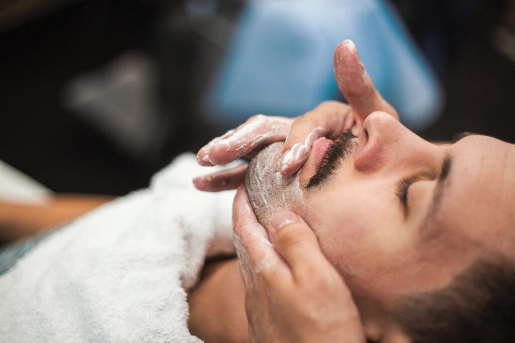 Blaireau chargé de mousse appliqué sur le visage d'un client chez le barbier