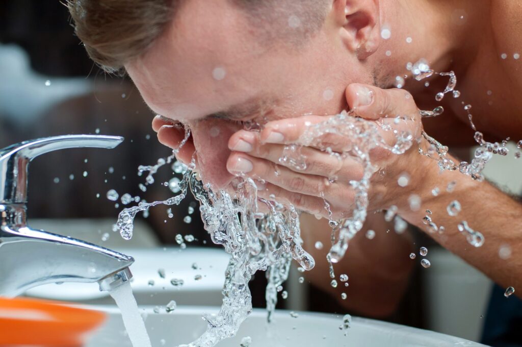 Homme qui se rince le visage à l'eau froide au-dessus d'un lavabo après son rasage